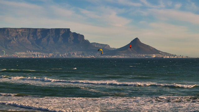 Aerial view of Table Mountain towers majestically over the city, its rugged peaks contrasting with the turquoise ocean where kitesurfers dance on the waves, Cape Town, Western Cape, South Africa.