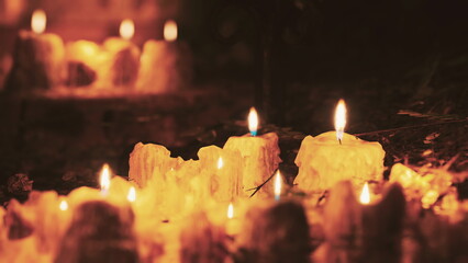 Flickering candles illuminate a serene space outdoors, casting warm light in the darkness. The soft glow enhances the peaceful ambiance as shadows dance around.