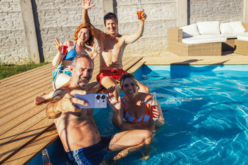 Group of friends relaxing in backyard pool having fun and making selfie with smart phone.