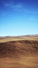 A serene view of a sprawling desert landscape showcases gentle hills and a bright blue sky. The horizon stretches far with earthy tones blending harmoniously, creating a sense of tranquility.