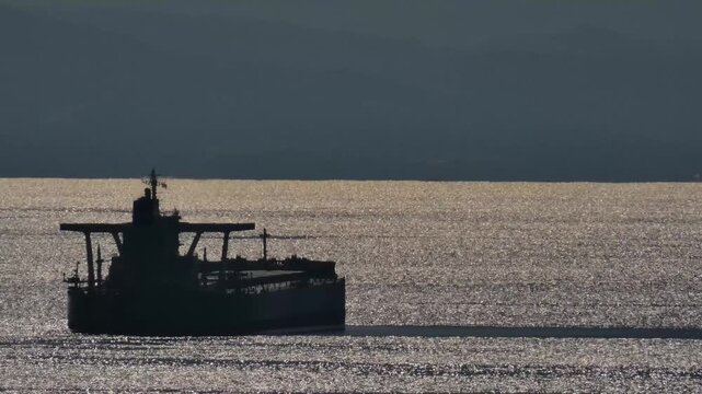 沖合の反射する海に停泊するタンカーのシルエット