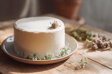 Delicate white cake adorned with flowers, set on a wooden surface in soft, natural light.