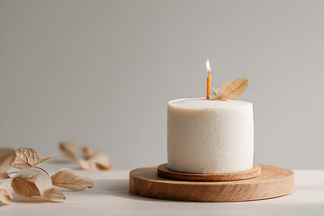 Minimalist cake with a single candle on a wooden stand, decorated with dried leaves.