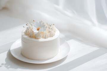 Delicate white cake adorned with a flower, presented on a white plate with soft lighting.