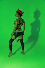 Obraz premium Full length portrait of young curly woman in leather lingerie with whip in her hands in green light