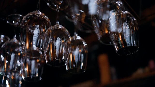 Close-up view of inverted wine glasses hanging on a bar rack, gleaming with reflections and warm bokeh lighting, showcasing elegant glassware in a dimly lit nightlife interior