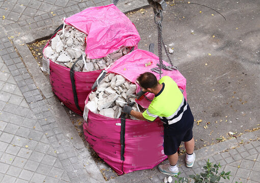 Saco de escombros de obra enganchado con gancho, cadena, garfio y eslinga por trabajador de gr&uacute;a