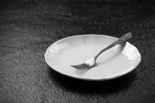 Empty plate and fork on dark stone surface showing the end of a meal and simple dining setting