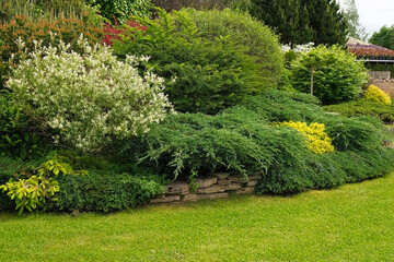 Frontyard Paver Walkway. Beautiful Ornamental Garden landscape design. Path made of natural stones, gravel. Landscaping modern trend. Lawn, shrubbery in the backyard. Abundance Of Plants Shrubs, Trees
