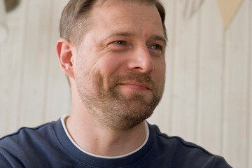 Fototapeta premium Handsome young man in blue jersey indoors. Male with stylish haircut, beard feel happy, calm and serious. Home interior background. Man looking to camera and into distance. Diversity People. Portrait