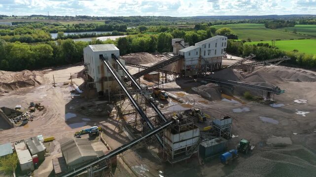 Aerial view of an aggregate processing plant with conveyors and machinery contrasting against green fields and a treeline, Nottingham, England, United Kingdom.