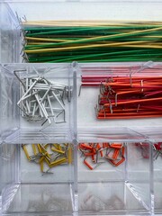 Color-coded jumper wires and electronic connectors organized in transparent plastic case, top-down macro shot