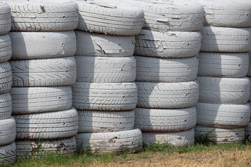 Stacked white tires forming a protective barrier and showing wear on a sunny day