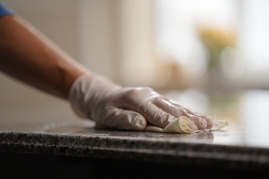 Gloved hand wipes a kitchen counter with a cleaning cloth