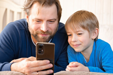 Father and son little boy laughing and using phone. They watching funny videos together, playing...