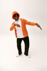 Young man showcases stylish orange outfit with playful energy in a modern studio setting