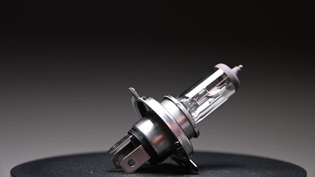 A halogen headlight h4 bulb for a car. This spare part for ambient lighting rotates on a black gradient background.