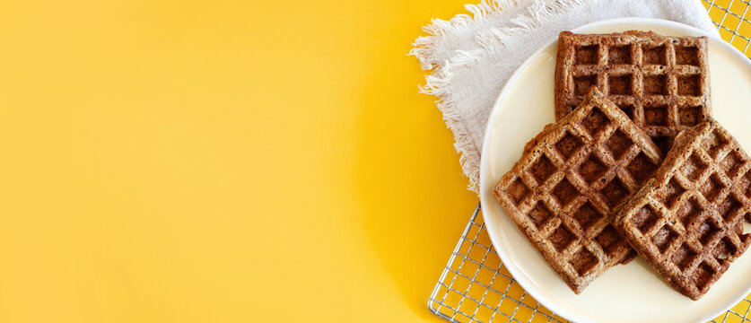 Homemade oat waffles on a white plate on a sunny yellow background copy space