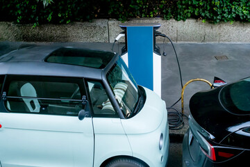 High Angle View of Two Compact Electric Vehicles Charging Side-by-Side at a Modern Blue Charging...