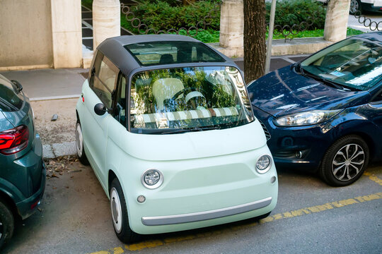 Modern Light Green Electric Microcar Parked in Urban Environment Between Traditional Vehicles in European City Street