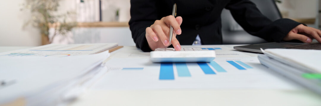 Financial Analysis. Businesswoman calculating data with calculator and laptop in modern office. - Powered by Adobe