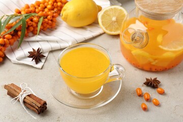 Sea buckthorn tea in glass cup, teapot, spices, lemon and fresh berries on light grey table, closeup