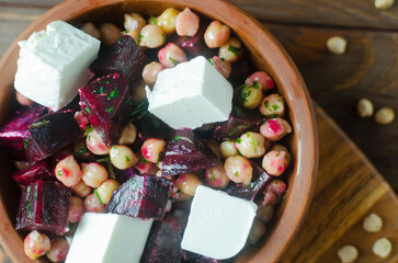 Beet Salad with chickpeas, feta and green sauce with oil and parsley in a ceramic bowl on a wooden table. Rustic style. Healthy eating. Horizontal orientation. Selective focus. Top view.