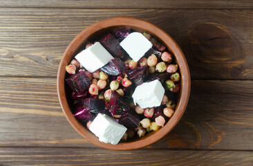 Beet Salad with chickpeas, feta and green sauce with oil and parsley in a ceramic bowl on a wooden table. Rustic style. Healthy eating. Horizontal orientation. Selective focus. Top view.