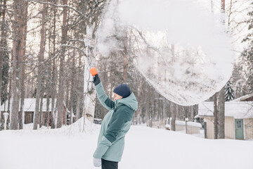 Teenager girl throwing boiling water into freezing air in a snowy forest in Lapland, creating a cloud of ice crystals