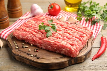 Raw minced meat with parsley and spices on wooden table, closeup