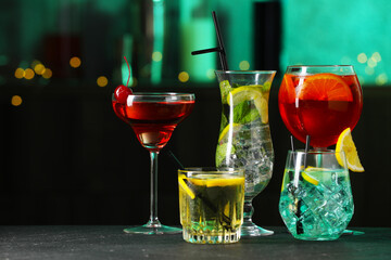 Glasses of tasty cocktails on dark table against blurred background, bokeh effect. Space for text