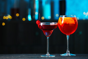 Glasses of tasty cocktails on dark table against blurred background, bokeh effect. Space for text
