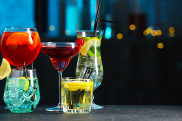 Glasses of tasty cocktails on dark table against blurred background, bokeh effect. Space for text