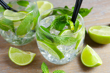 Glasses of tasty cocktails with limes and mint on wooden table, closeup