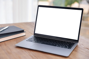Laptop with empty white screen and stationery on desk in room. Comfortable home workplace