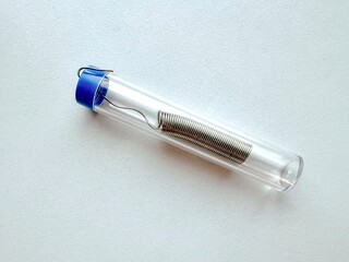 Coiled solder wire stored in transparent plastic tube with blue cap, isolated on white background