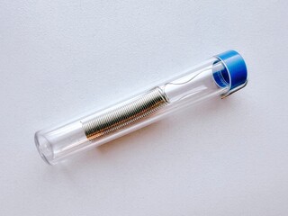 Coiled solder wire stored in transparent plastic tube with blue cap, macro close-up on white background