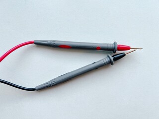 Red and black multimeter test probes with sharp metal tips on light background, electrical measuring tools