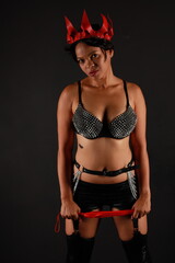 Low key portrait of pretty young dark haired woman in leather lingerie with whip in her hands