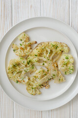 Cauliflower with chimichurri sauce on a white plate on a white wooden background. Concept of vegan and vegetarian food. Healthy eating. Vertical orientation. Selective focus. Top view