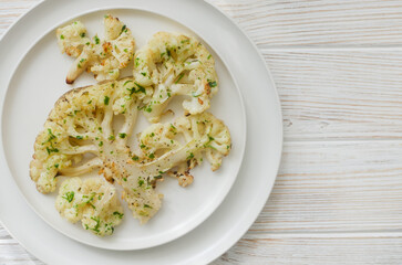 Cauliflower with chimichurri sauce on a white plate on a white wooden background. Concept of vegan and vegetarian food. Healthy eating. Horizontal orientation. Selective focus. Top view. Copy space