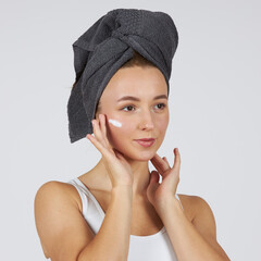 A young beautiful girl in white underwear with a towel on her head uses cosmetic face cream.