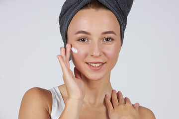 A young beautiful girl in white underwear with a towel on her head uses cosmetic face cream.