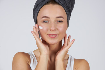 A young beautiful girl in white underwear with a towel on her head uses cosmetic face cream.