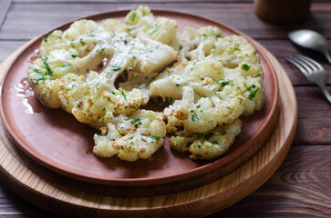 Cauliflower with chimichurri sauce on a ceramic plate on a wooden background. Concept of vegan and vegetarian food. Healthy eating. Vertical orientation. Selective focus.