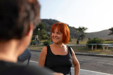 Women of different ages chat animatedly on the street outside the gym after a group Pilates class