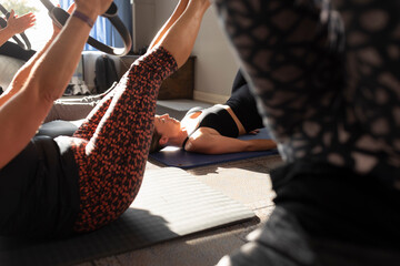 A young woman does Pilates exercises in a small gym, alongside other women