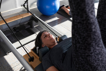 A woman does Pilates exercises on a reformer machine during a Pilates class at a gym