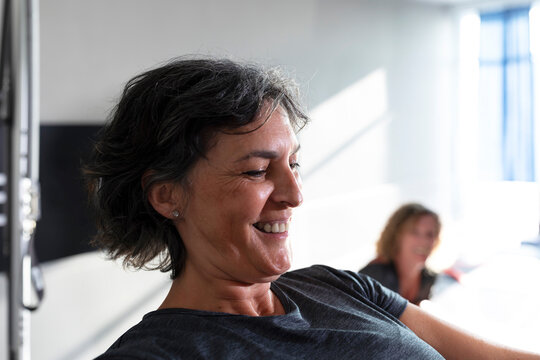 An elderly woman smiles happily while doing Pilates exercises on a reformer machine during a Pilates class - Powered by Adobe