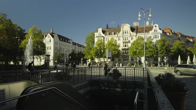 A sunny autumn day at Prinzregentenplatz in Bogenhausen, Munich, Germany. Cyclists, pedestrians, and transport meet historic architecture in this German city. Fountain, theater, U-Bahn entrance